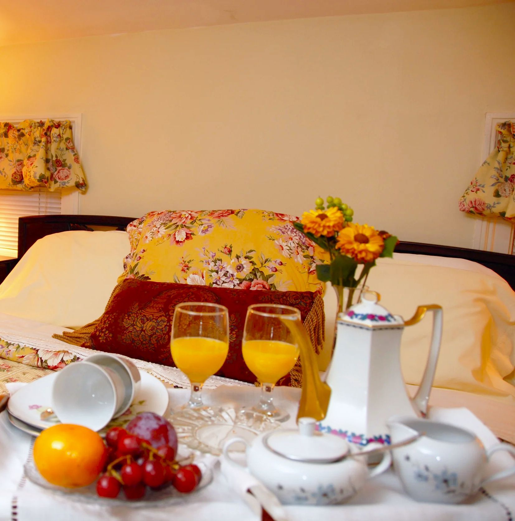 Two glasses of orange juice sit on a table in front of a bed
