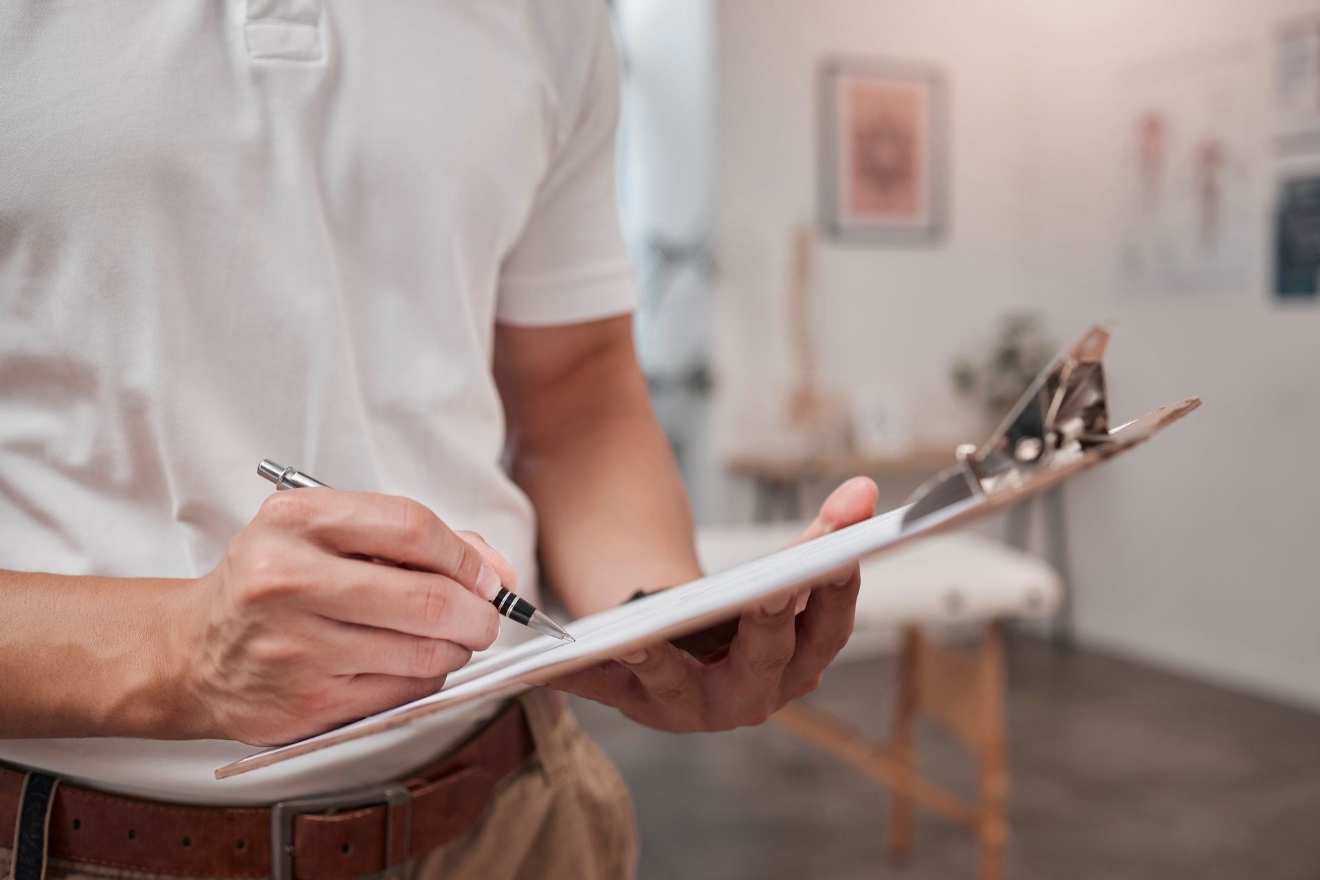 Person in white shirt writing on a clipboard in a medical office.