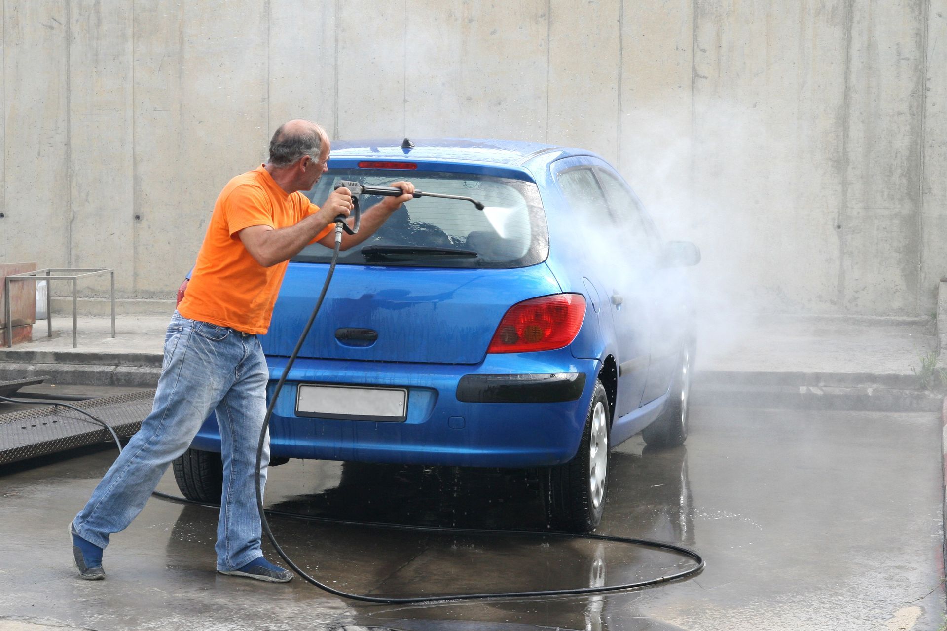 A man is washing a blue car with a high pressure washer