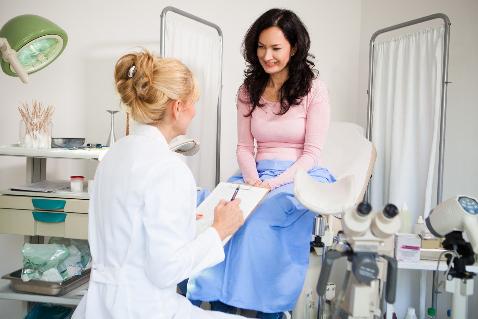 Una donna è seduta su una sedia ginecologica e parla con un medico.