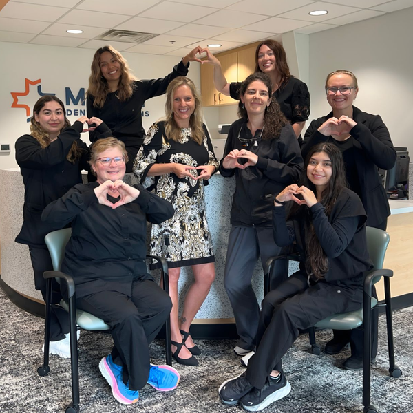 Office group smiling and forming heart shapes with their hands, standing and sitting together.