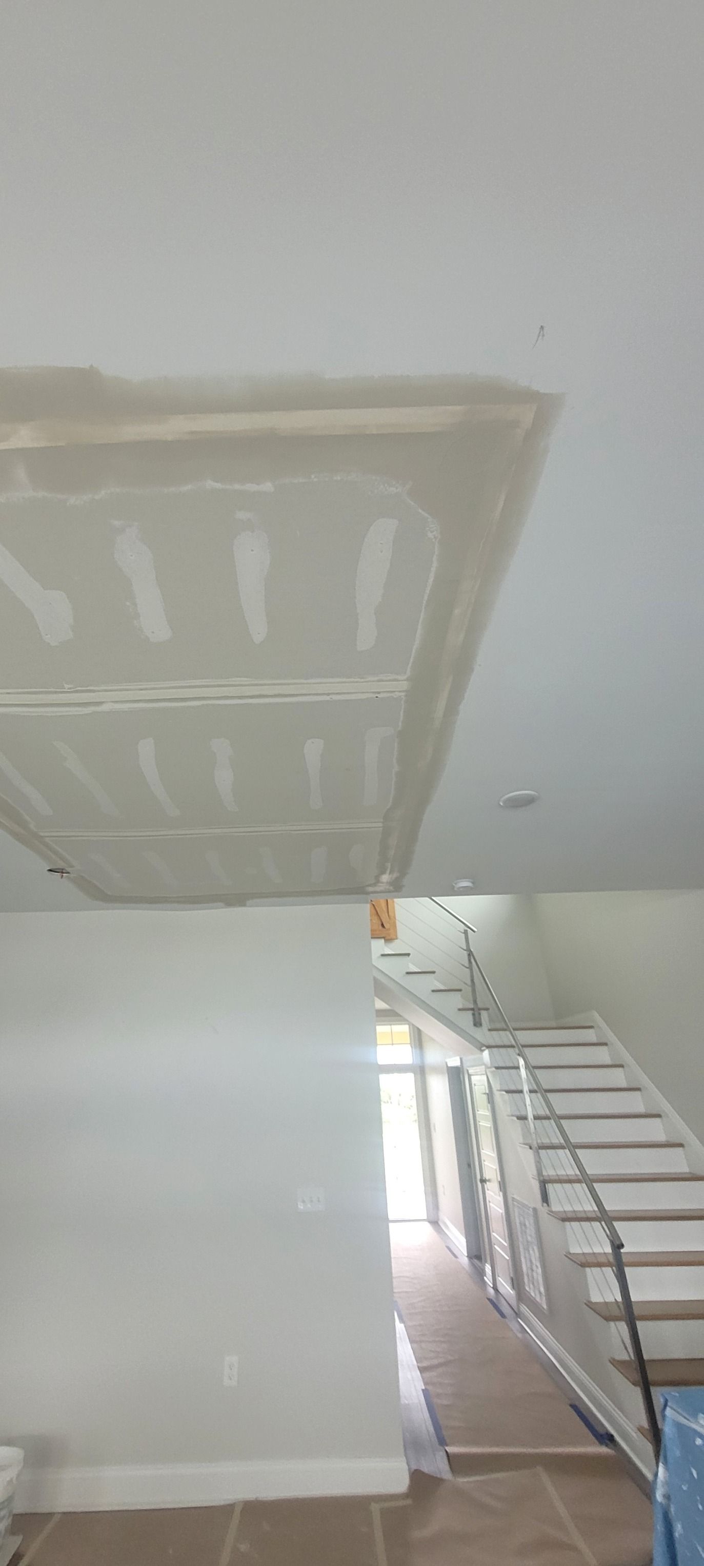 Interior view with unfinished drywall ceiling feature and staircase. White walls, construction paper on floors.