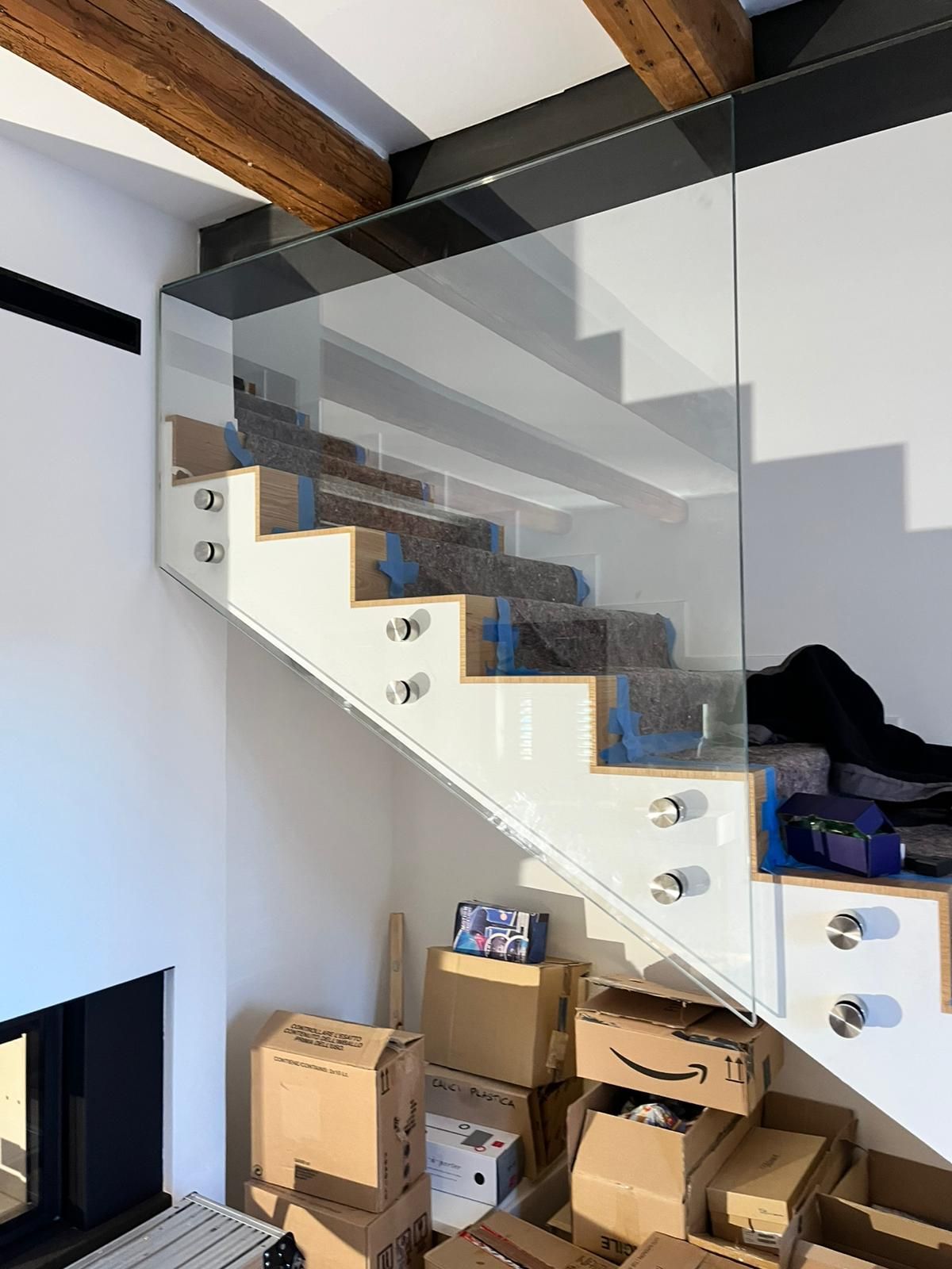 Scala moderna con gradini bianchi e ringhiere in vetro, parzialmente ostruita da scatole di cartone e materiale da imballaggio.