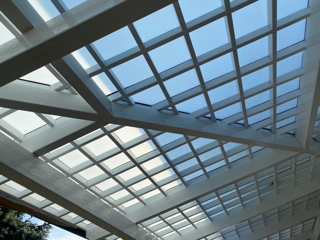Una struttura a pergola bianca con tetto a griglia in vetro si staglia contro un cielo azzurro limpido.