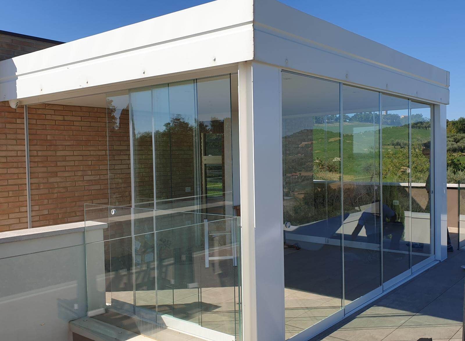 Una moderna pergola bianca con pareti in vetro su un patio in pietra adiacente a un muro di mattoni.