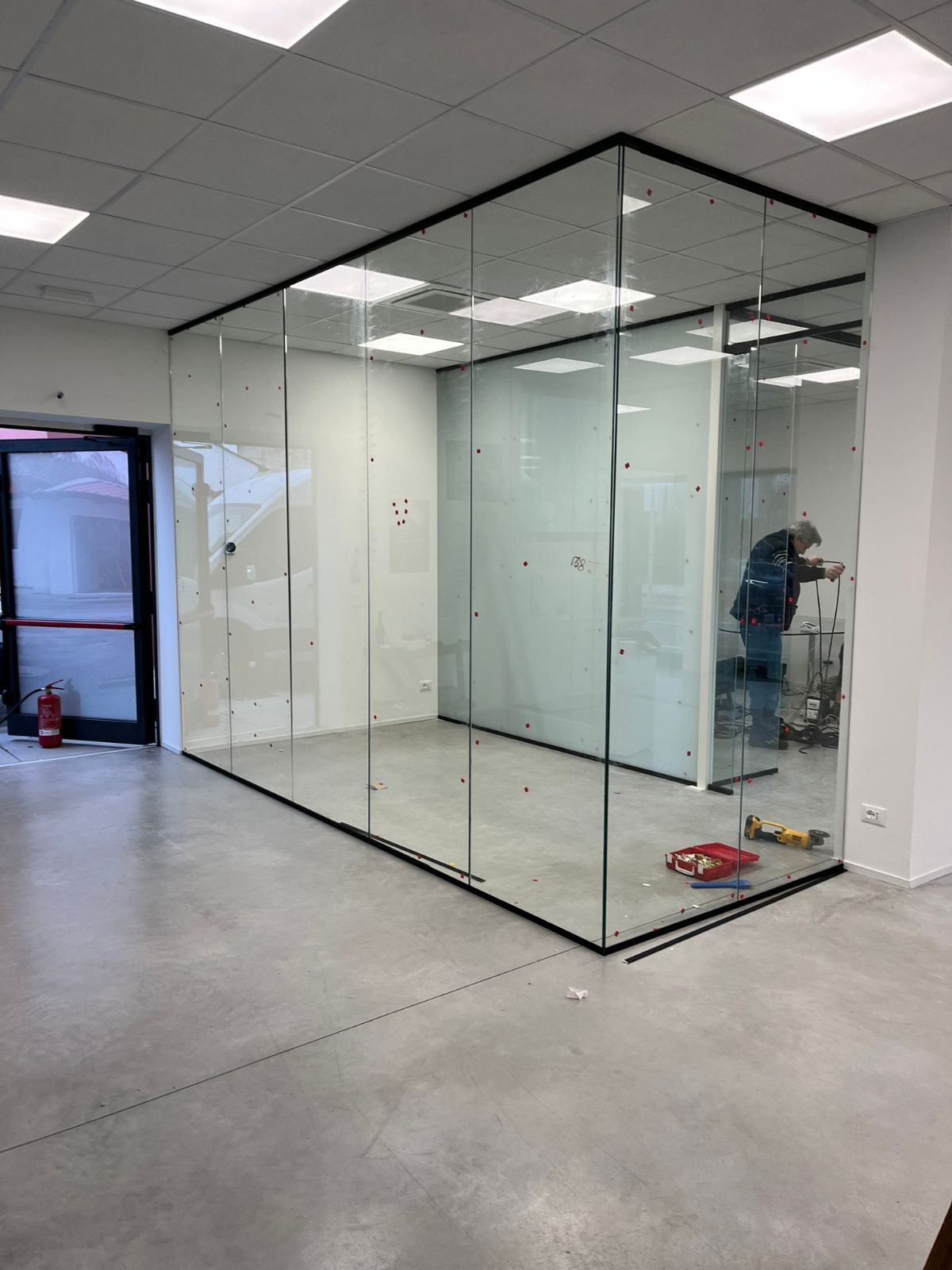 Interno di un ufficio con un cubicolo con pareti in vetro appena installato, in fase di completamento da parte di un operaio.