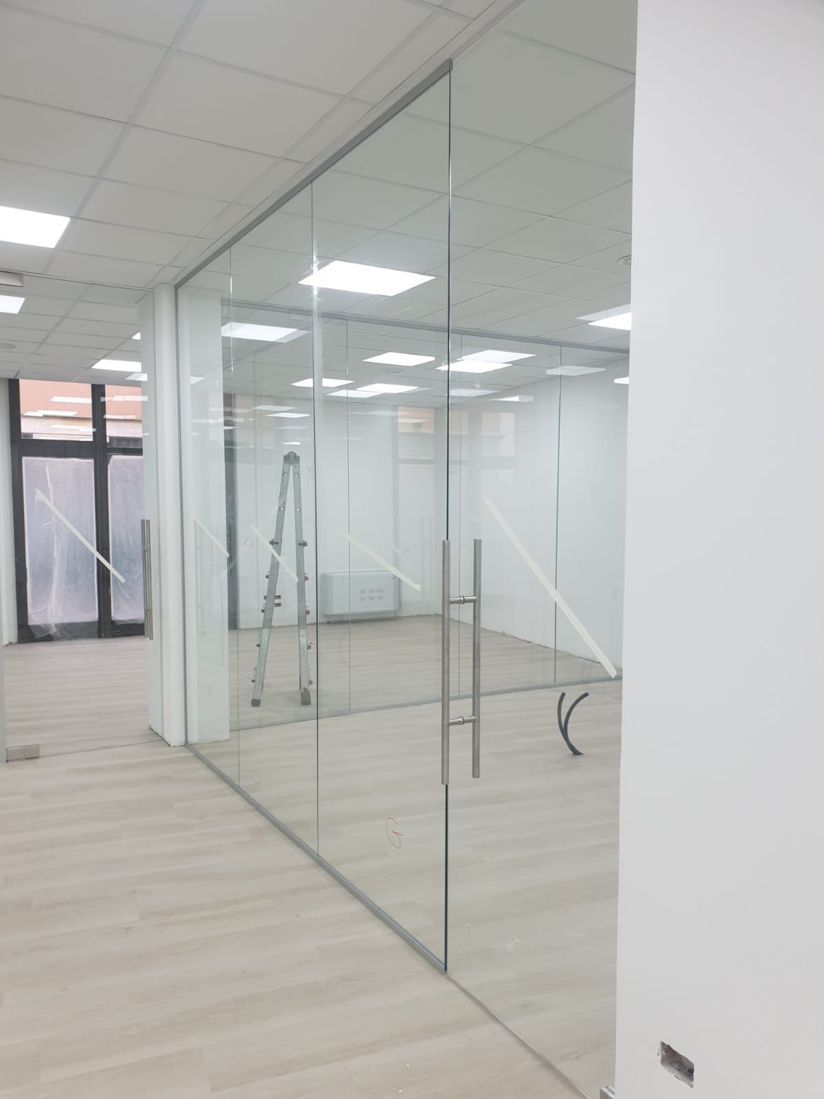 Spazio ufficio moderno con ampie pareti divisorie in vetro, una porta d'ingresso in vetro con maniglie argentate e una scala interna.