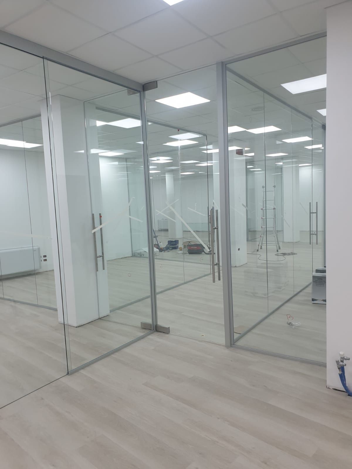Interni di ufficio moderni caratterizzati da sale riunioni con pareti divisorie in vetro, pareti bianche e pavimenti con effetto legno chiaro.