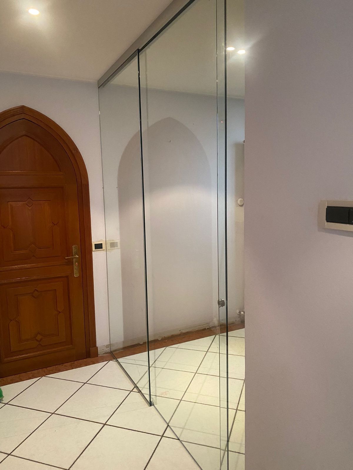 Un corridoio caratterizzato da una porta ad arco in legno sulla sinistra e da un'ampia parete a specchio che si estende dal pavimento al soffitto sulla destra.