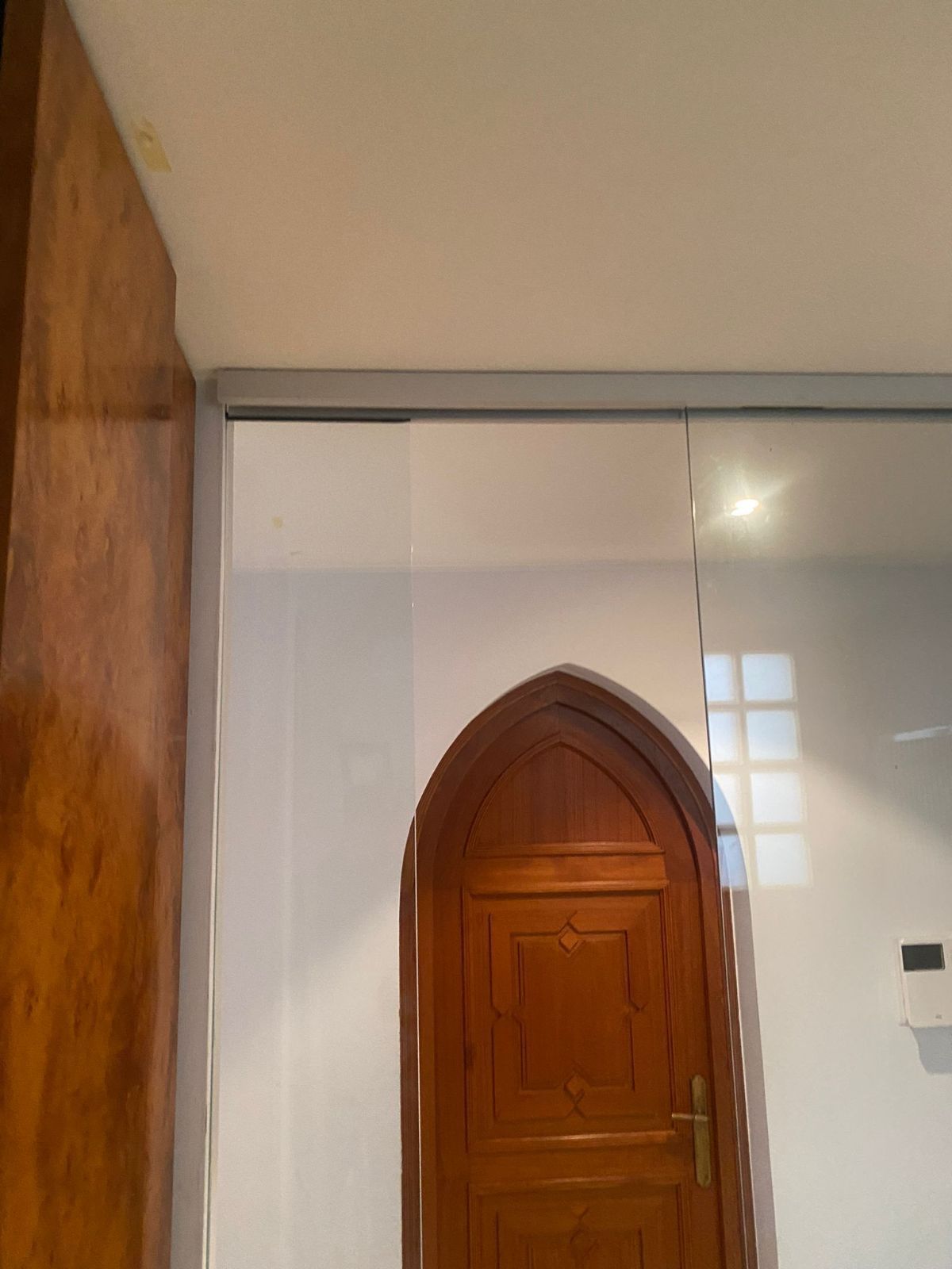 Una porta ad arco in legno incastonata in una parete con pannelli a specchio riflettenti, vista da un'angolazione leggermente dall'alto.