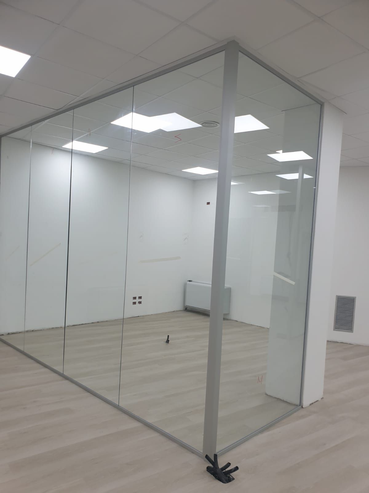 Una parete divisoria in vetro con telaio metallico installata in un ambiente luminoso e moderno con pavimento chiaro.
