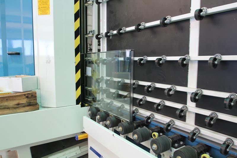 Una lastra di vetro poggia sui rulli di una macchina industriale per la lavorazione del vetro.