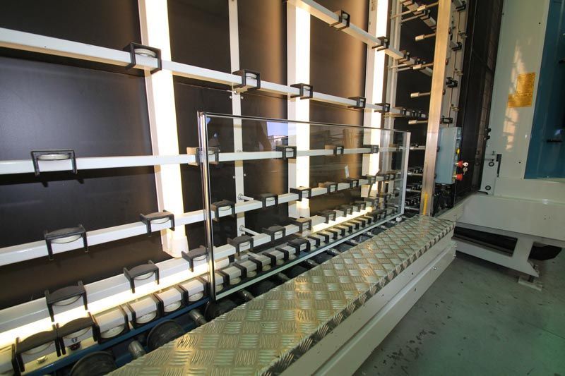 In un ambiente industriale, su uno sfondo scuro, si trova una scaffalatura verticale per la movimentazione del vetro, completa di rulli e staffe.