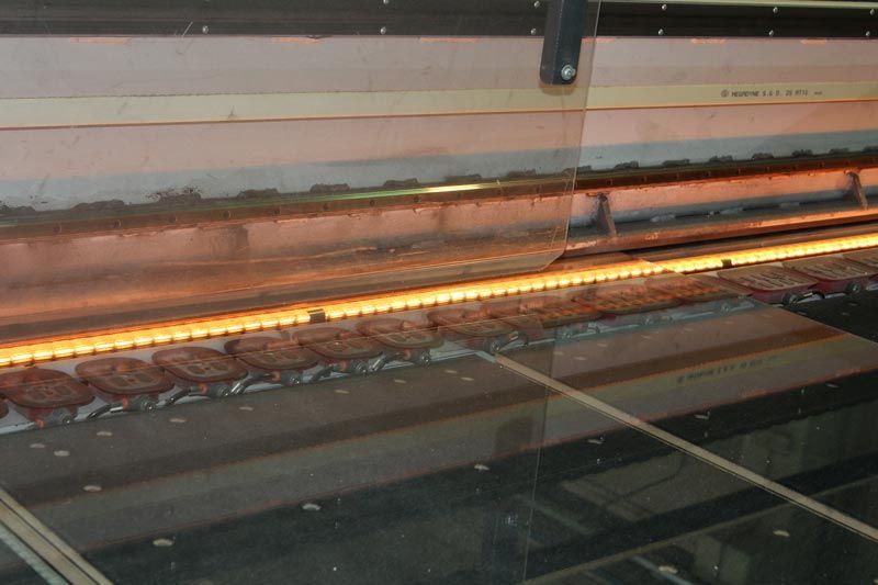 Una fila di componenti metallici incandescenti che si muovono lungo una catena di montaggio industriale all'interno di una fabbrica.