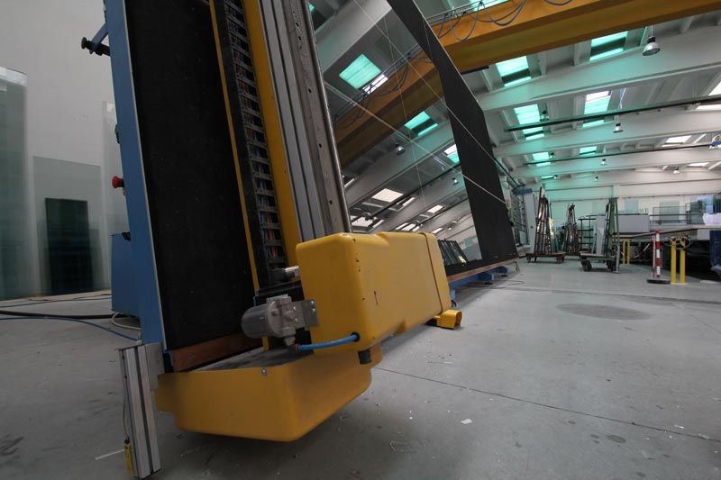 In un luminoso capannone industriale si erge una macchina gialla per il taglio del vetro.
