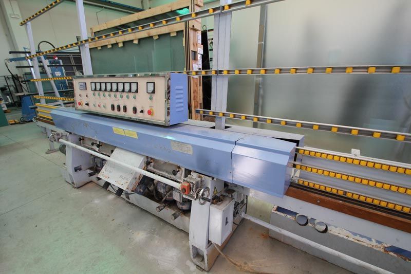 In un'officina è presente una lucidatrice per bordi del vetro a più mandrini di colore azzurro chiaro, dotata di un pannello di controllo con quadranti analogici.