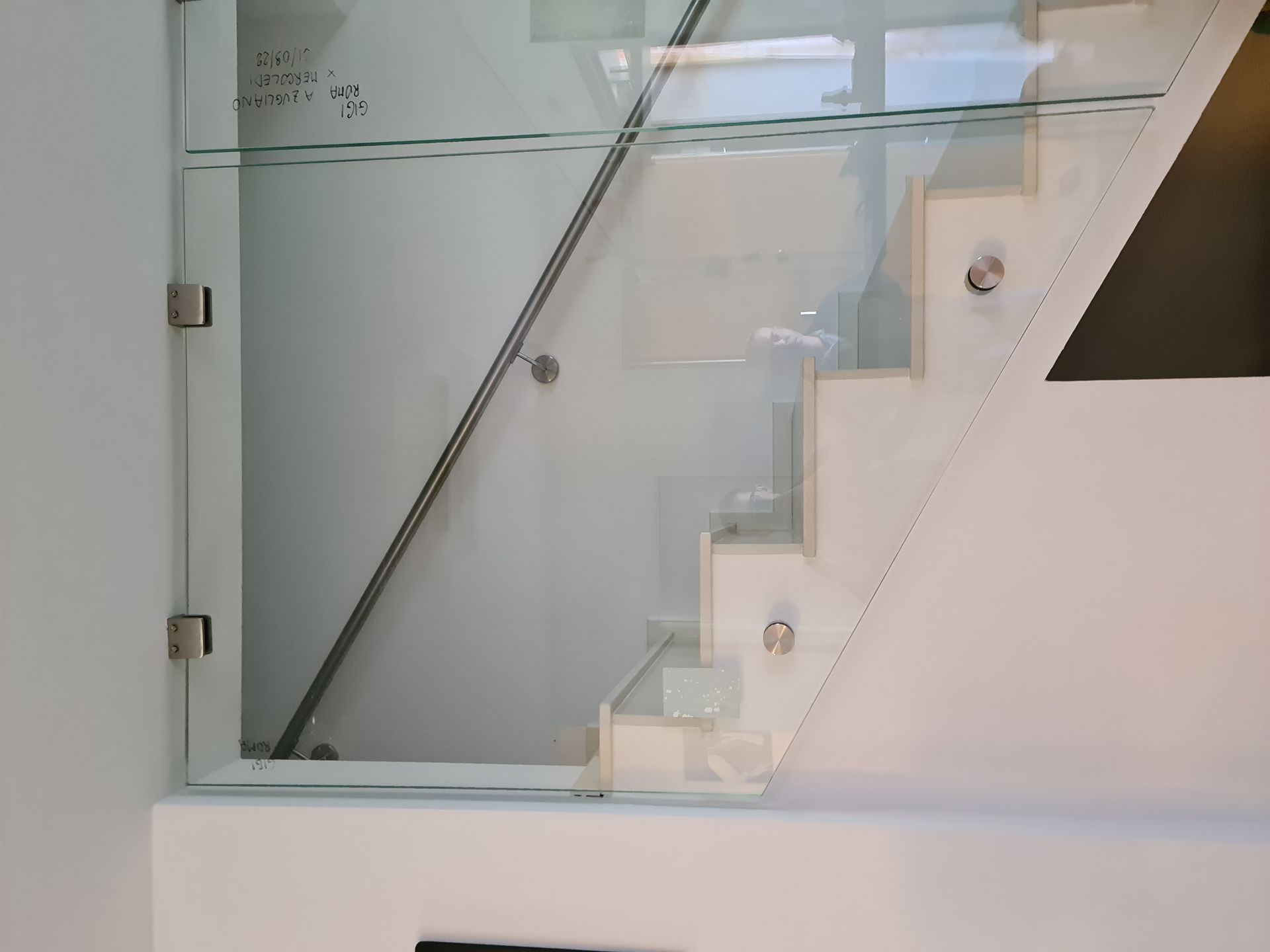 Ringhiera in vetro con distanziatori in acciaio inox lungo una moderna scala bianca con corrimano in metallo.