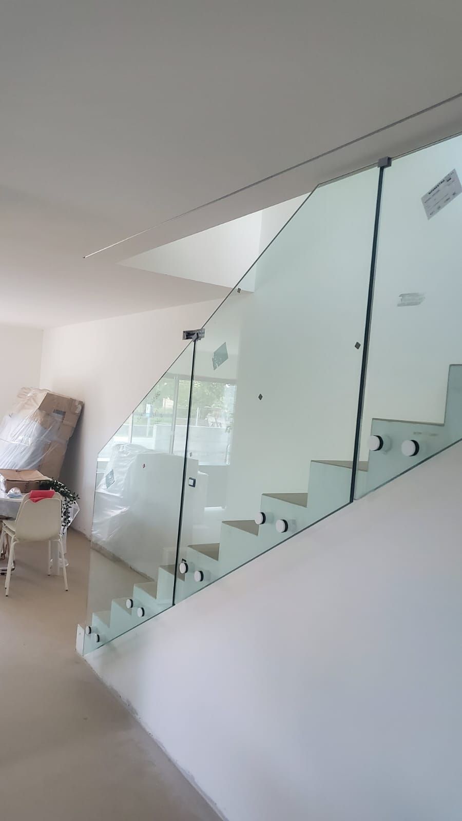 Una scala moderna con ringhiera in vetro senza telaio, fissata con distanziatori metallici, in una casa minimalista bianca.