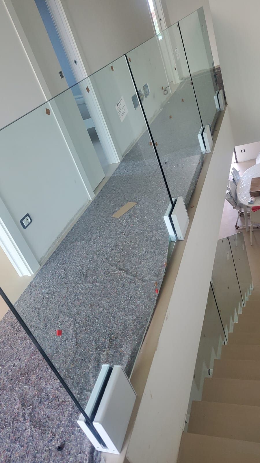 Una ringhiera in vetro con elementi in metallo argentato, installata su un balcone che si affaccia su una scala con pavimento di colore chiaro.