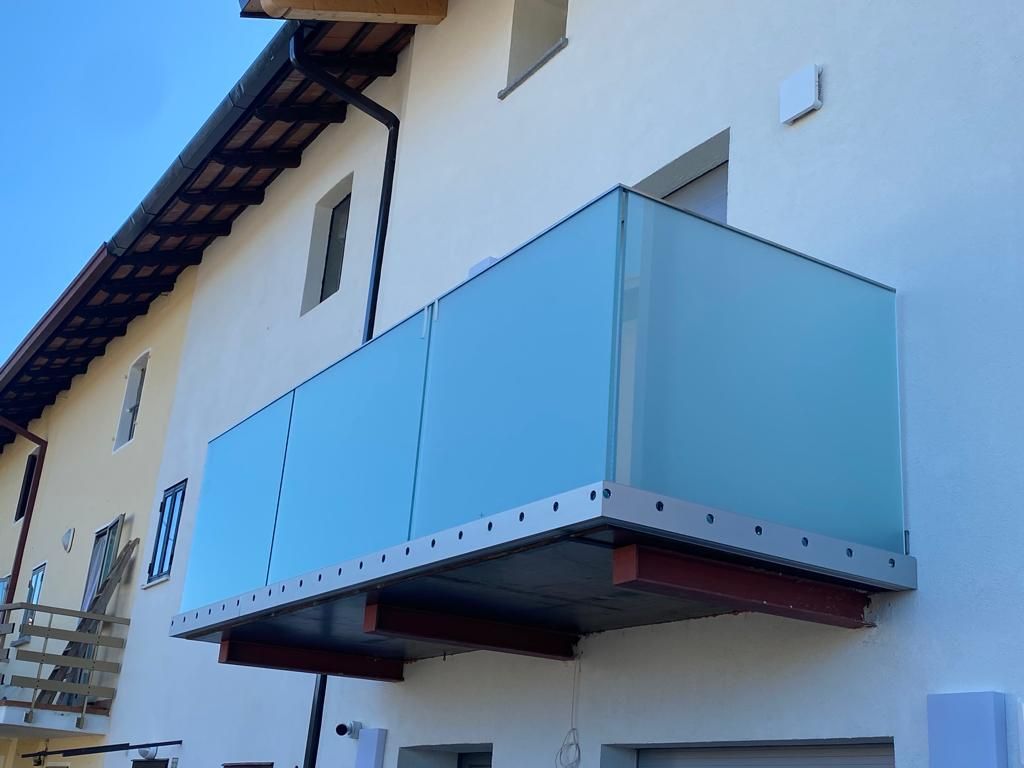 Un balcone moderno con pannelli in vetro satinato e struttura metallica, che si estende dal lato di un edificio residenziale bianco.