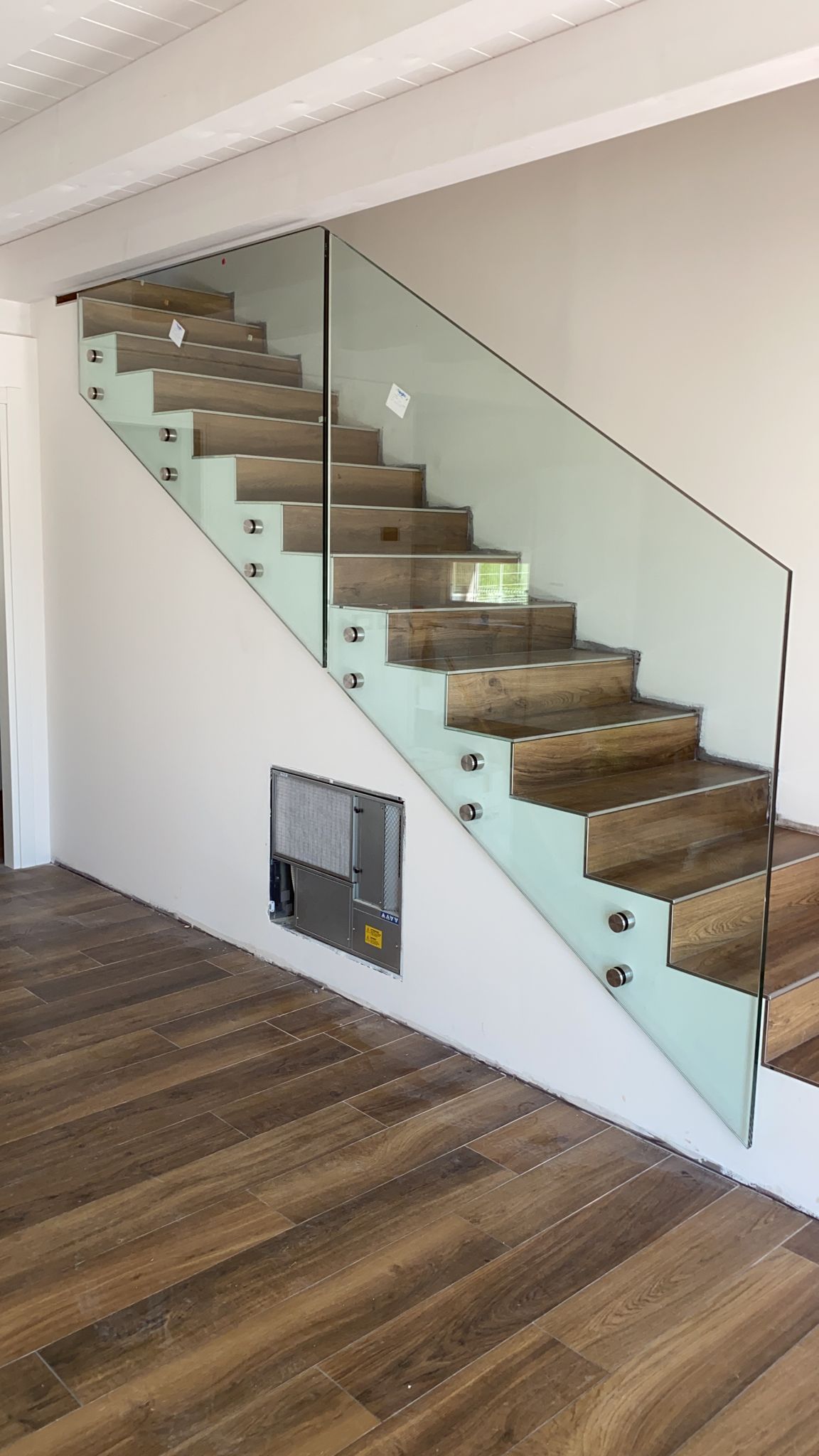 Scala moderna in legno con ringhiera in vetro senza telaio montata lateralmente, incastonata su una semplice parete bianca.