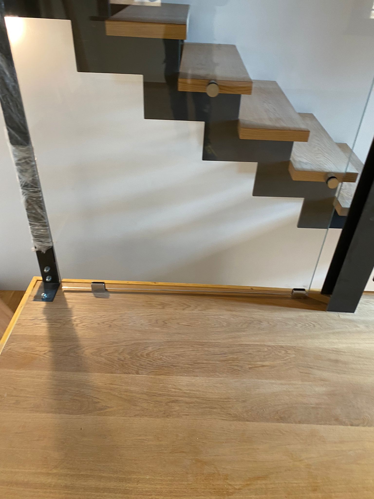 Primo piano di una scala in legno con gradini a vista, ringhiera in vetro e struttura di supporto in metallo nero, su uno sfondo bianco.