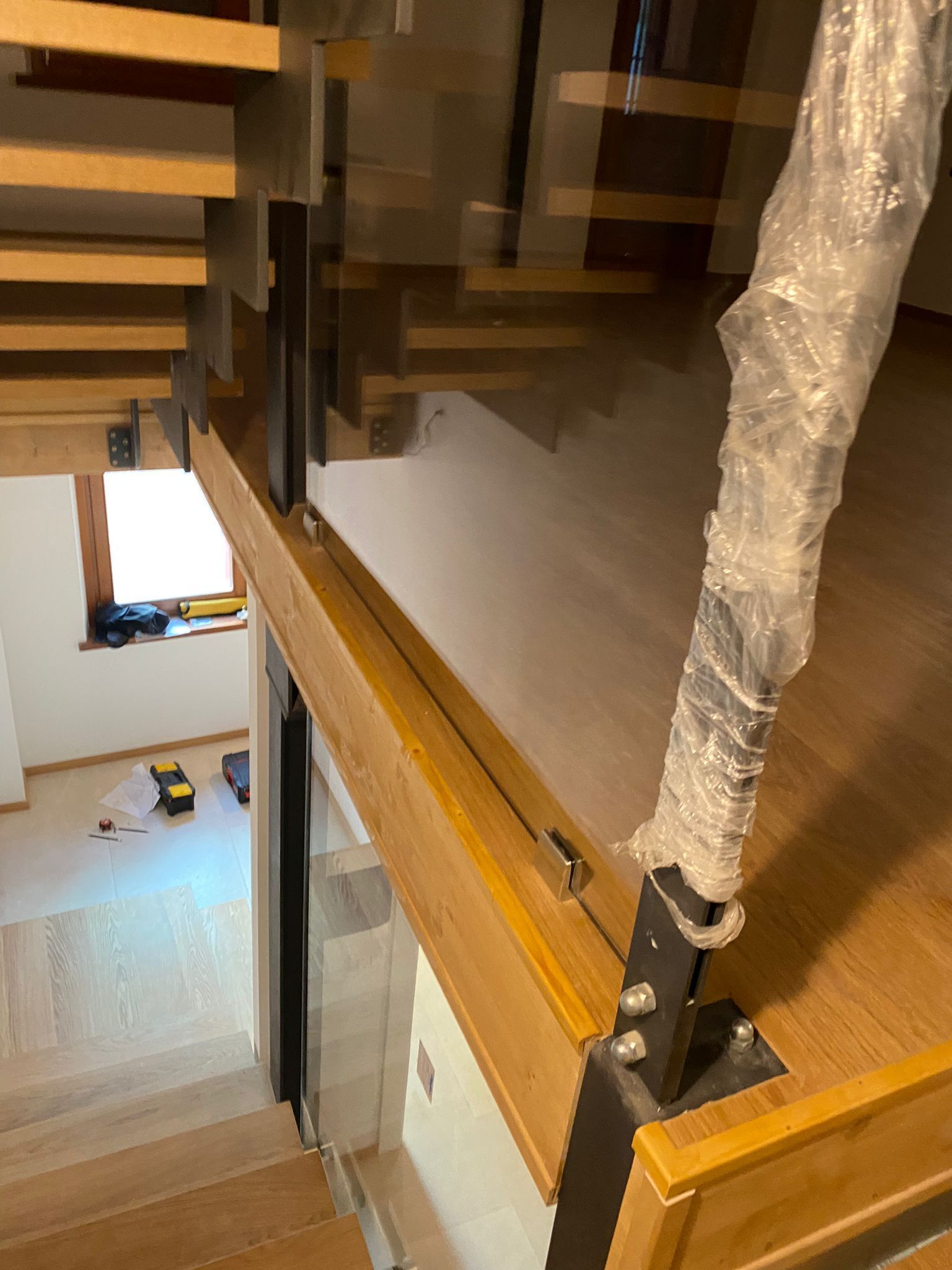 Una scala in legno in costruzione con un montante del corrimano in metallo avvolto nella plastica, vista dal pianerottolo superiore.