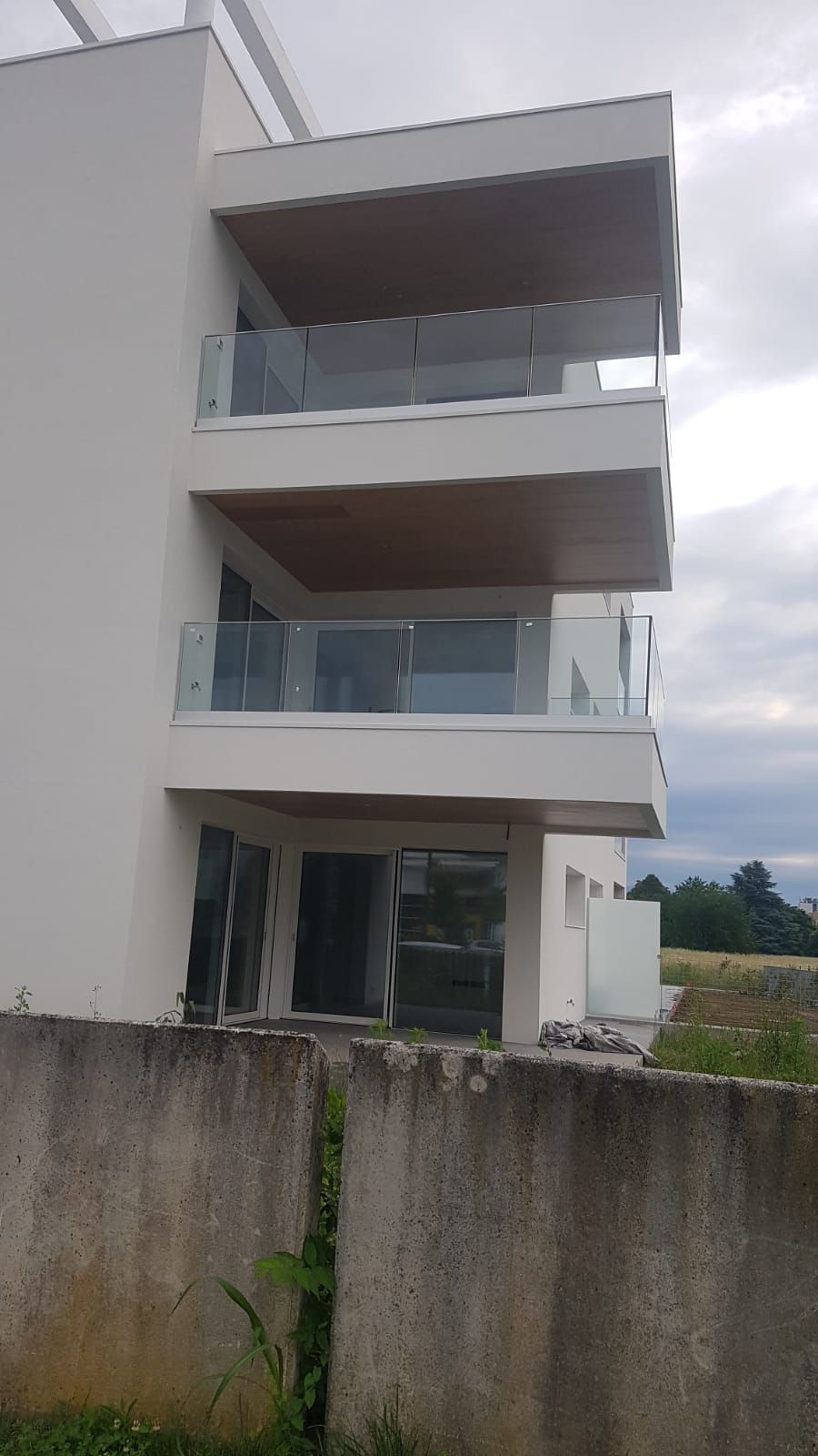 Un moderno edificio a tre piani con balconi bianchi sovrapposti, ringhiere in vetro e pannelli inferiori marroni.