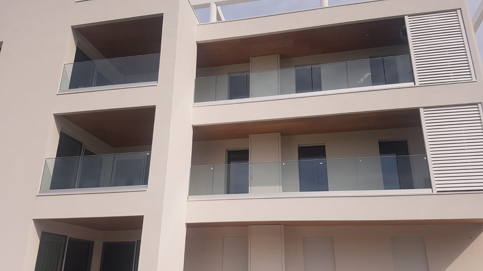 Moderno edificio residenziale a più piani con facciata beige, balconi con vetrate e pannelli decorativi bianchi.