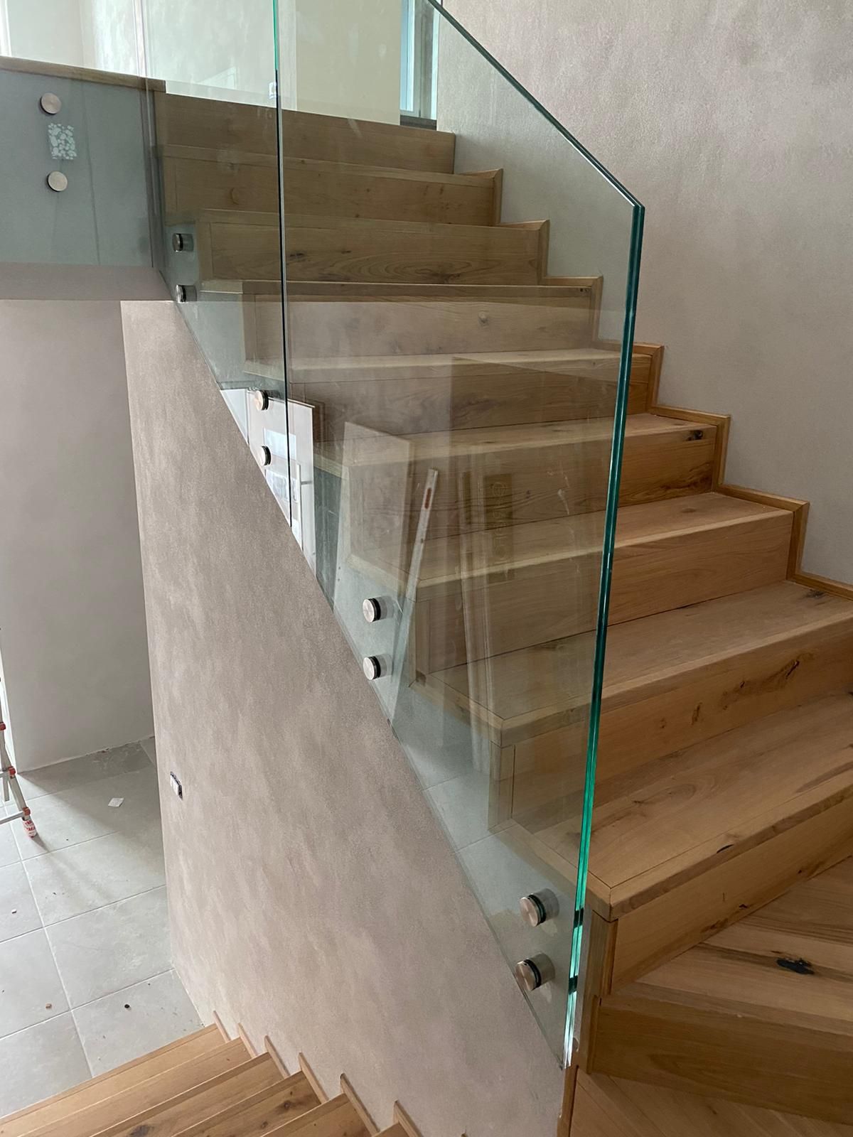 Scala moderna in legno con ringhiera in vetro senza telaio fissata lateralmente con elementi metallici.