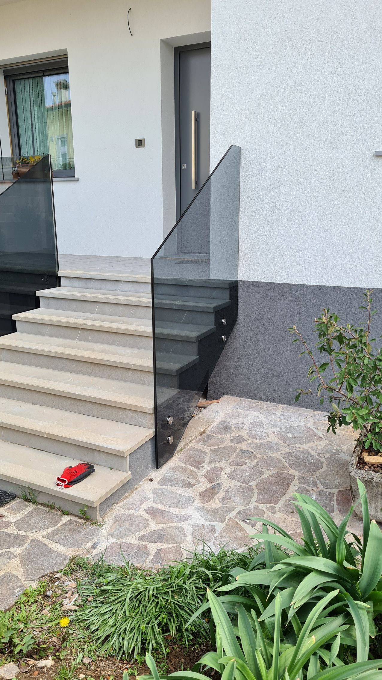 Una scalinata in pietra conduce a una porta d'ingresso con una ringhiera in vetro fissata lateralmente.
