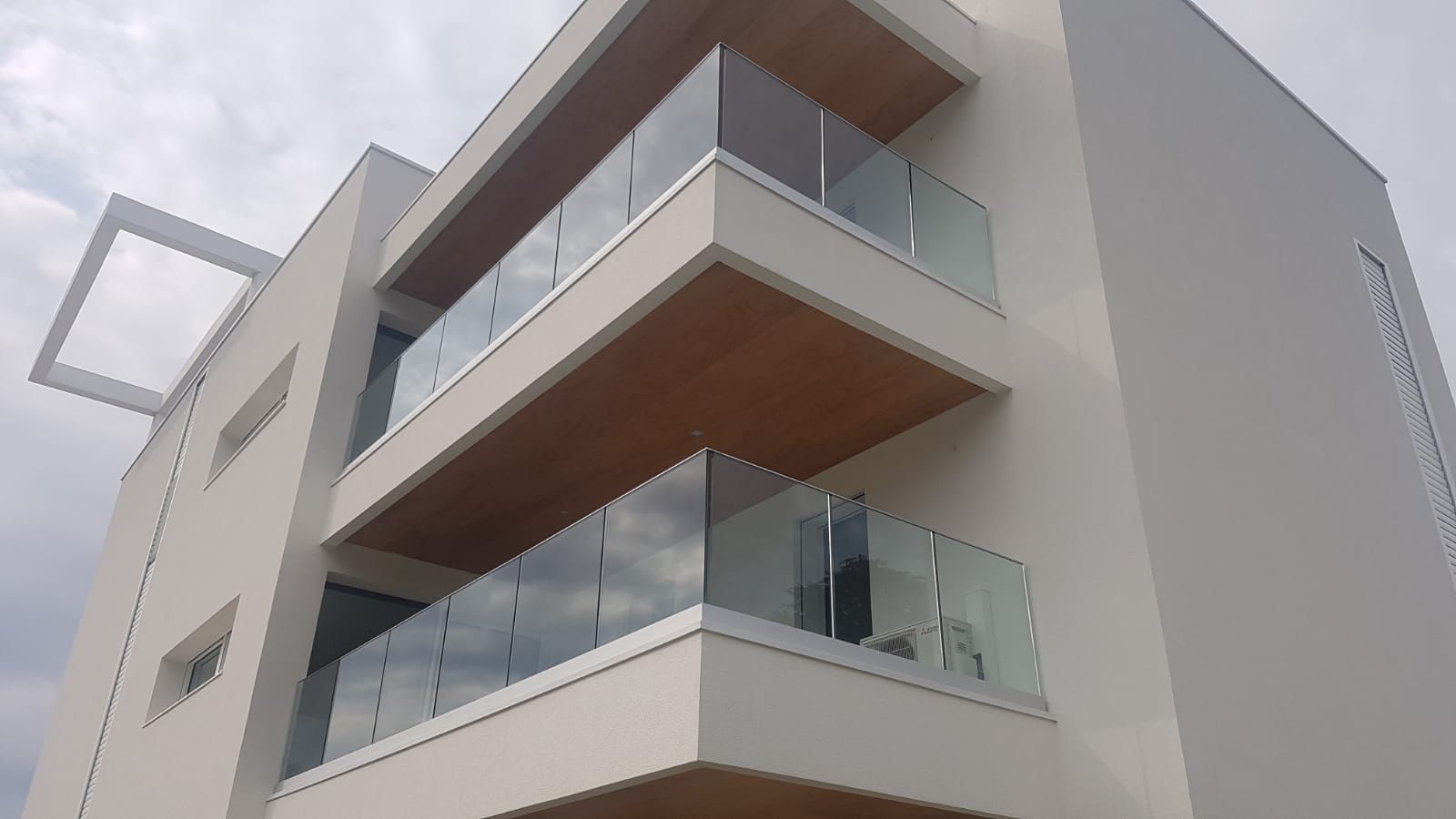 Una vista dal basso di un moderno edificio residenziale bianco con balconi sovrapposti dotati di ringhiere in vetro e soffitti in legno.