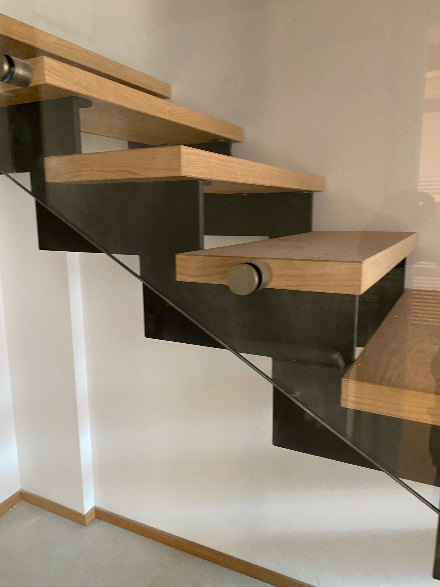 In un interno moderno, i gradini in legno sospesi sono fissati a una trave centrale in metallo scuro con ringhiera laterale in vetro.