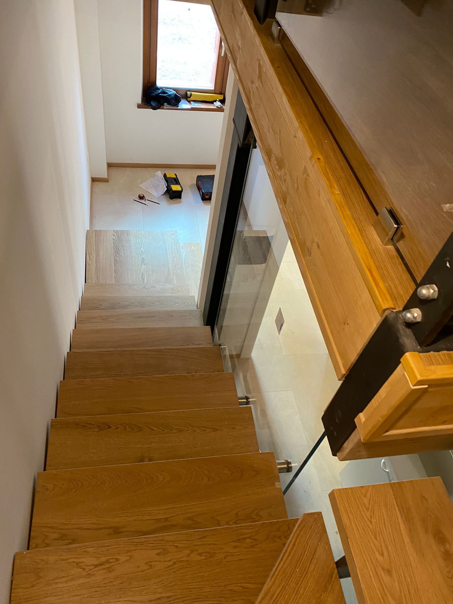 Una vista dall'alto di una scala di legno che conduce a una stanza con una finestra e attrezzi da costruzione sul pavimento.