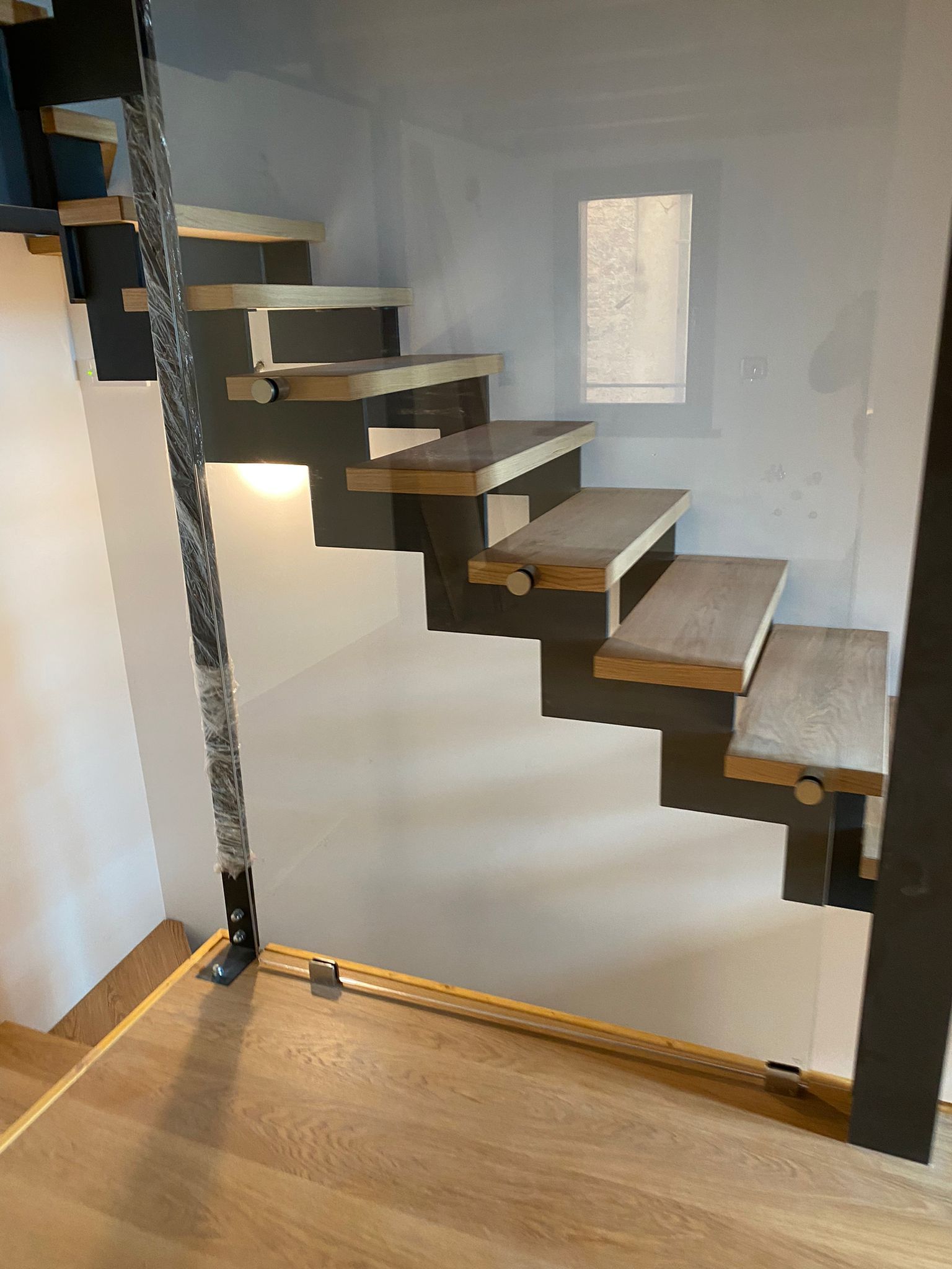 Moderna scala sospesa in legno con supporti strutturali grigio scuro e corrimano decorativo in corda in una stanza bianca.