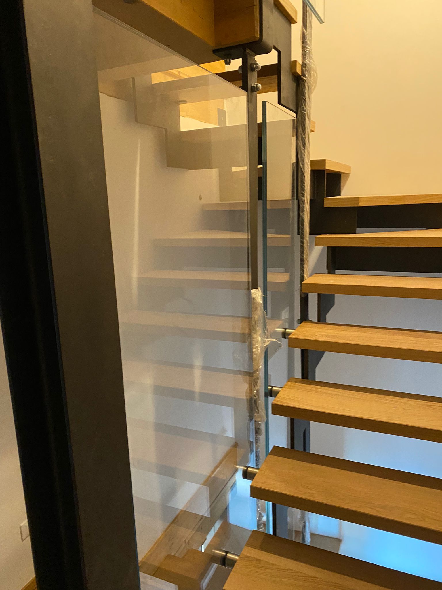 Una scala con gradini in legno e una moderna ringhiera in vetro sorretta da montanti metallici.