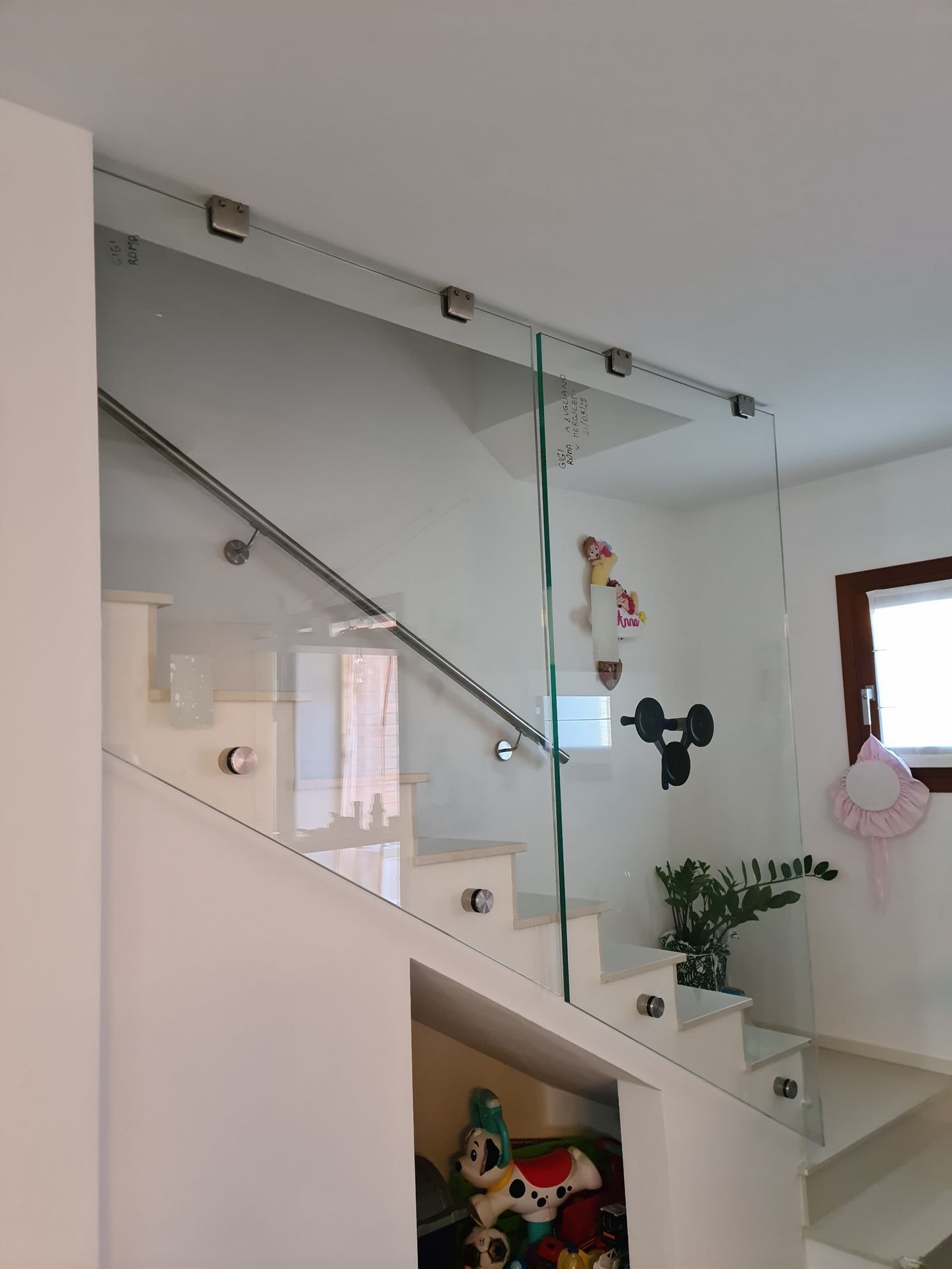 Una scala con ringhiera in vetro e corrimano in acciaio, dotata di uno spazio contenitore aperto sottostante, pieno di giocattoli.