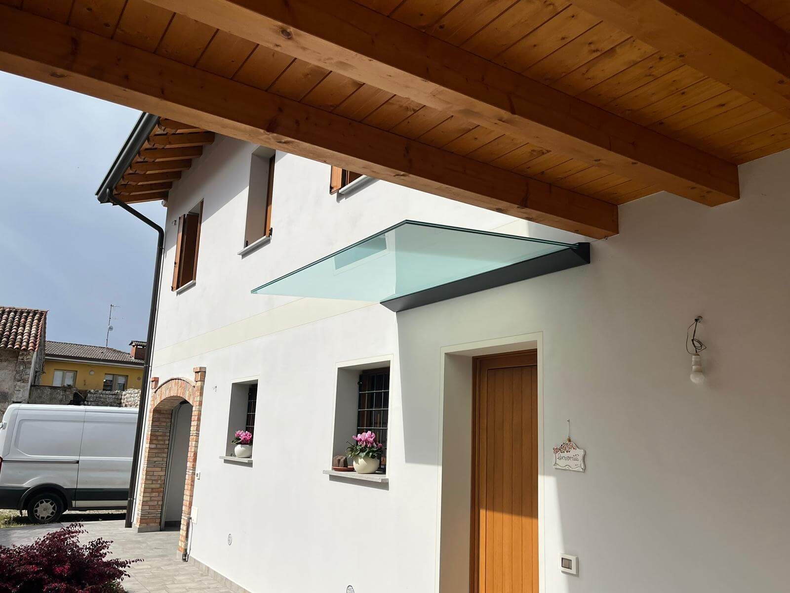 Un edificio bianco con una sporgenza del tetto in legno e una moderna pensilina in vetro sopra una porta d'ingresso in legno.