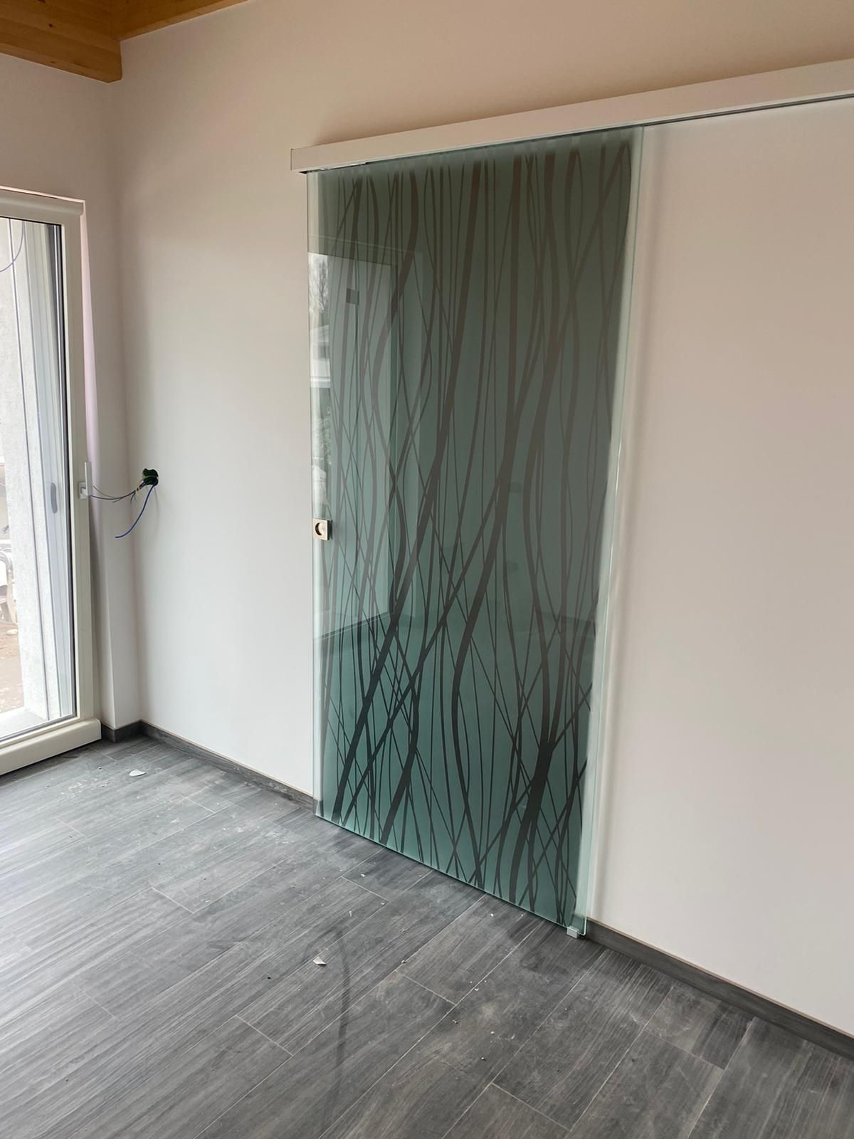 Una porta scorrevole in vetro con un motivo a rami d'albero neri e satinati, installata in una stanza con pareti bianche e pavimento grigio.