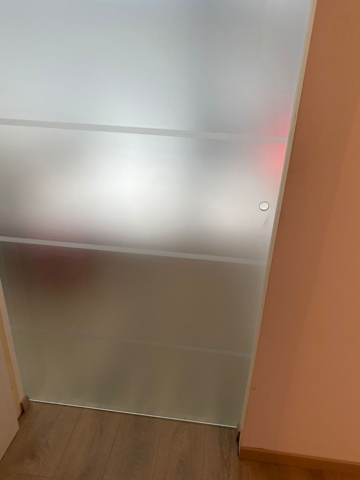 Una porta scorrevole in vetro satinato con strisce orizzontali opache, posizionata in una stanza con pareti chiare e pavimento in legno.