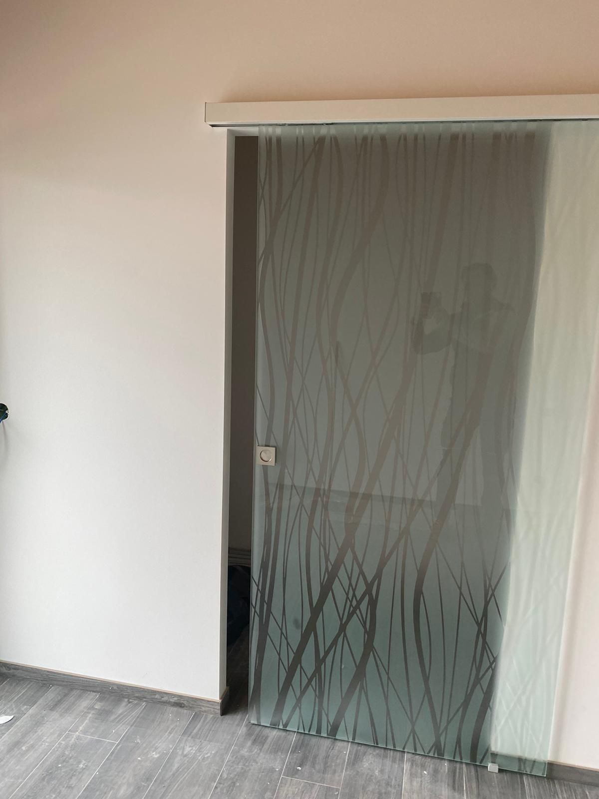 Una porta scorrevole in vetro satinato con un delicato motivo a rami scuri, montata su un binario bianco all'interno di una stanza.