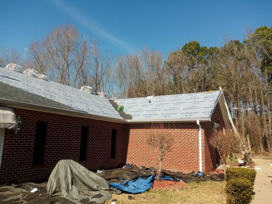 Brick house with damaged roof and tarps in a backyard under a clear blue sky