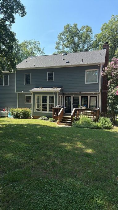 Gray two-story house with a small porch, white trim, and a grassy yard under trees