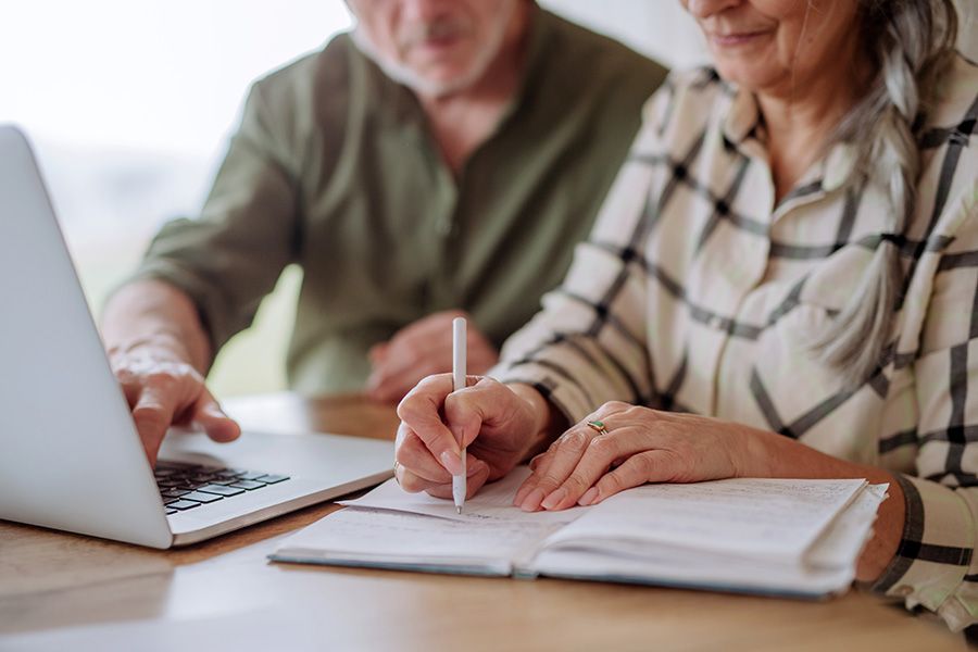 Elderly couple making checklists for funeral, cremation arrangements up close with just focus on table and arms