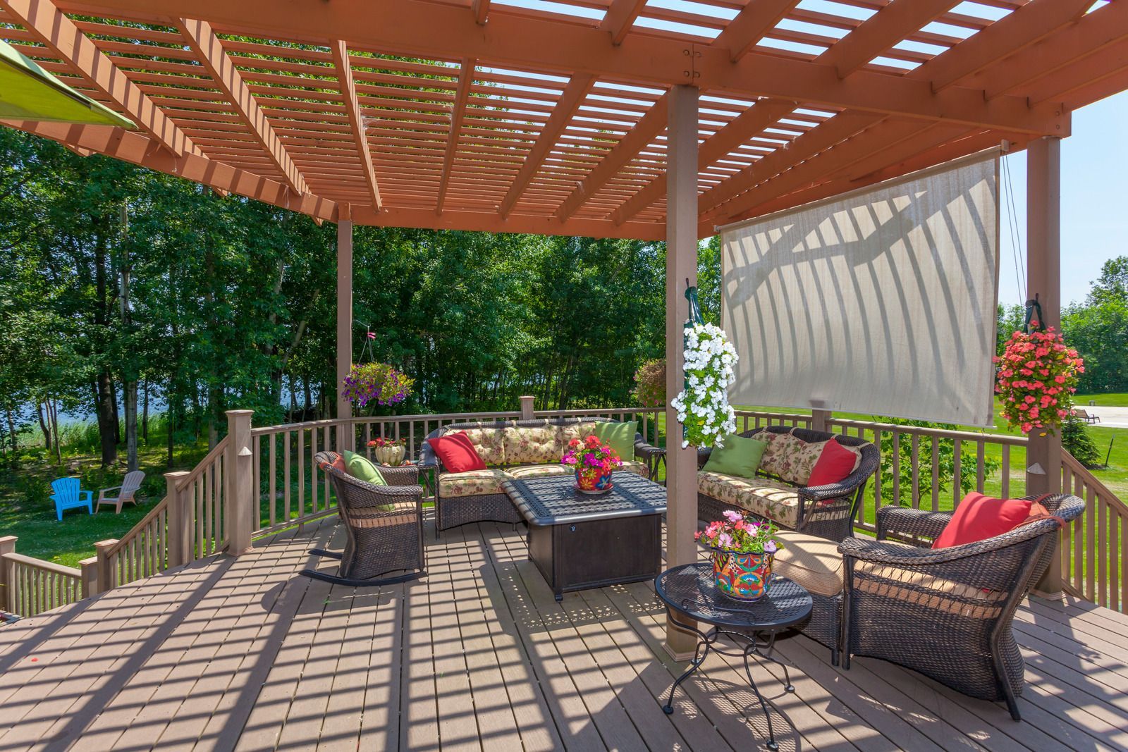 Covered backyard patio with wicker seating, patterned rug, and flower pots under a wooden pergola
