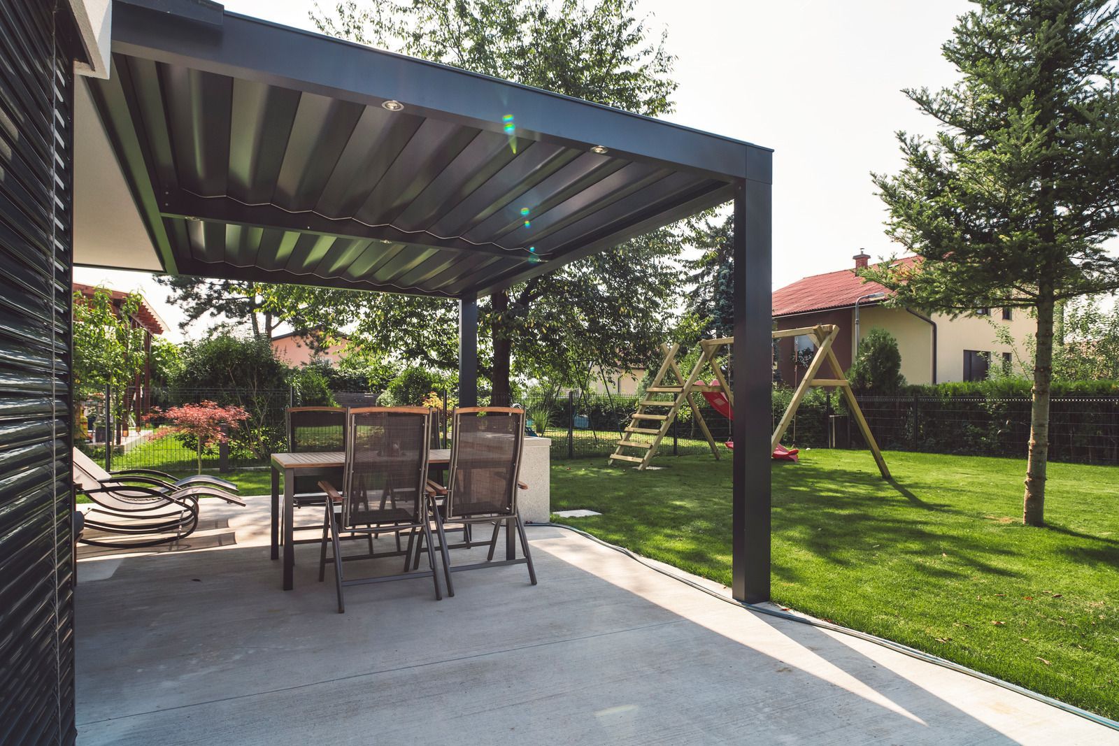 Covered patio with outdoor dining table and chairs beside a green backyard lawn