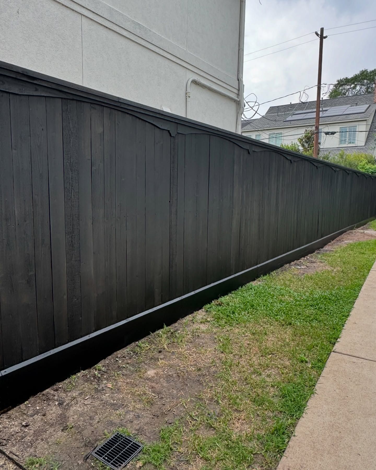 Long black fence beside a narrow grass strip and sidewalk next to a building