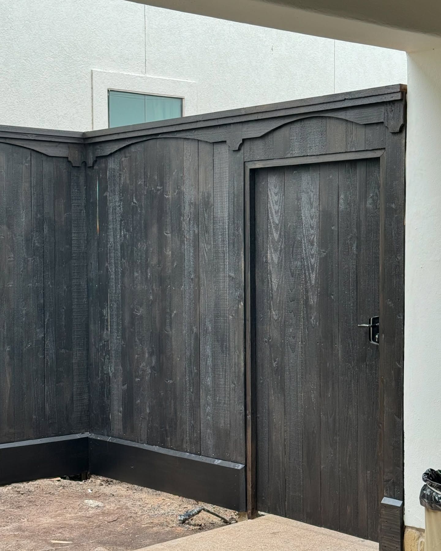 Dark wooden garden gate and fence beside a white stucco wall and gravel path