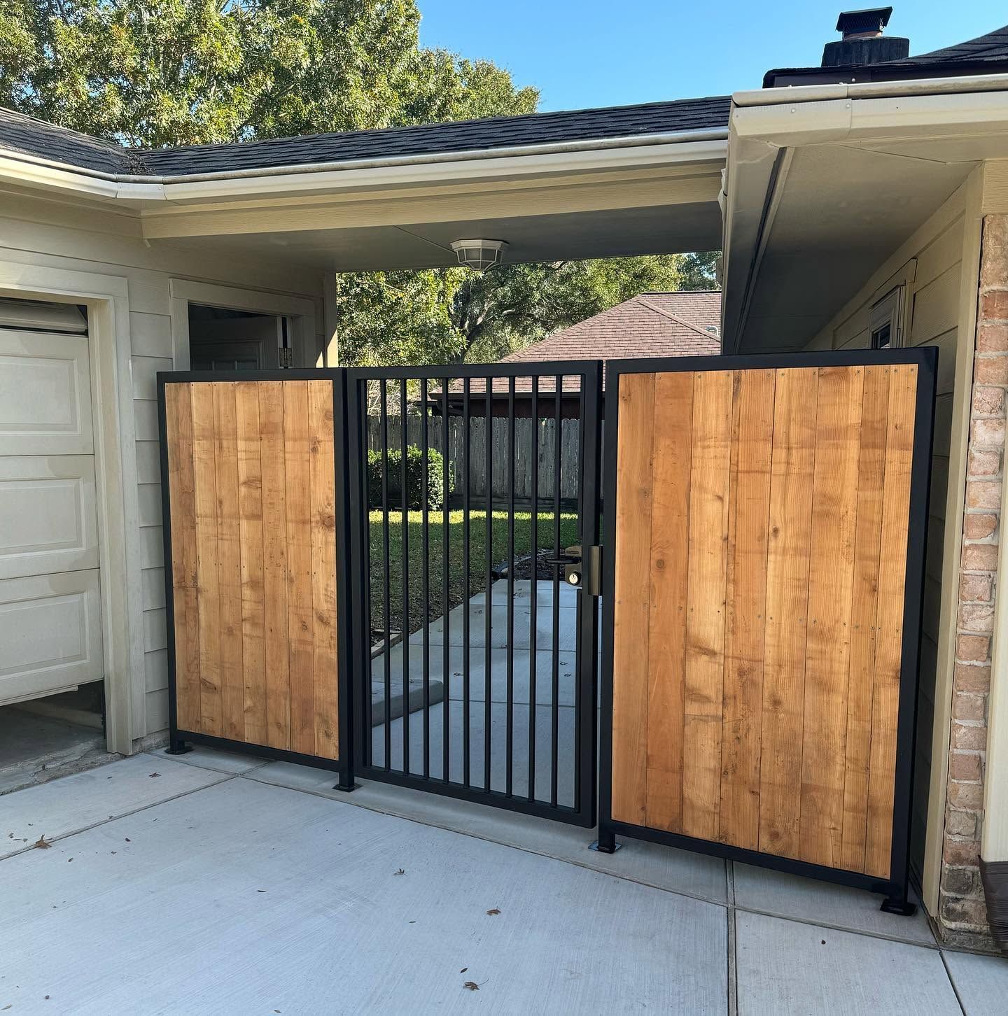 Black metal gate with wood privacy panels between a garage and house driveway