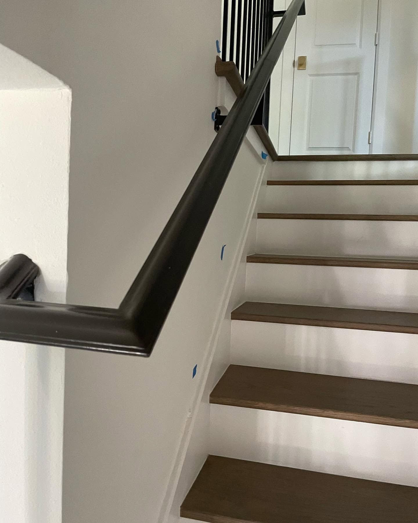 Indoor staircase with white walls, dark handrail, and wooden steps, viewed from the bottom.